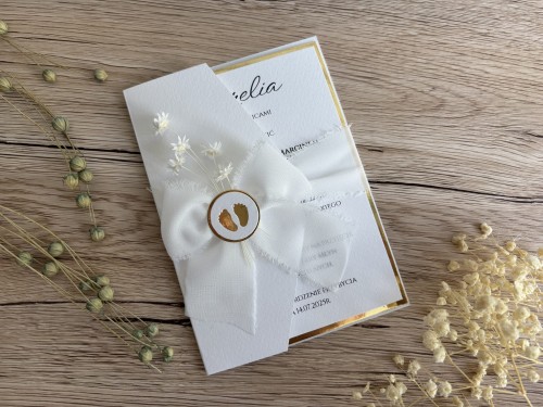 Zaproszenie na chrzest ozdobione szyfonową kokardką, suszonymi kwiatami i aplikacja ze stópkami.