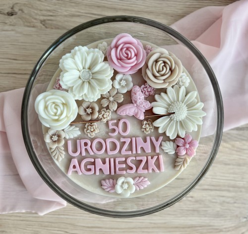 Świeca z wosku sojowego, dekorowana misternie wykonanymi kwiatami z wosku w odcieniach różu, beżu i bieli.